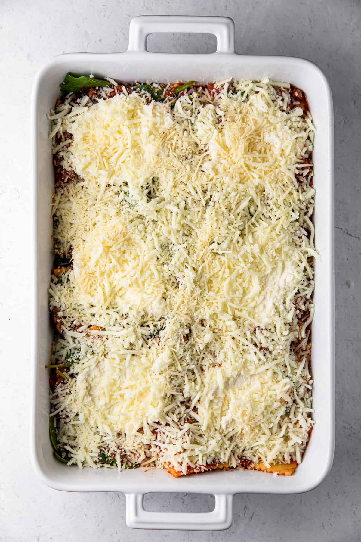 casserole dish with ravioli mixture, ricotta and shredded cheeses