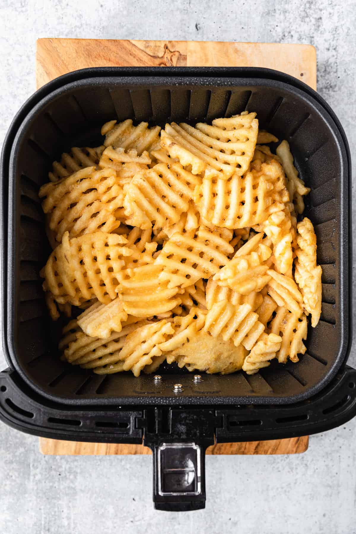 frozen waffle fries in the basket of an air fryer