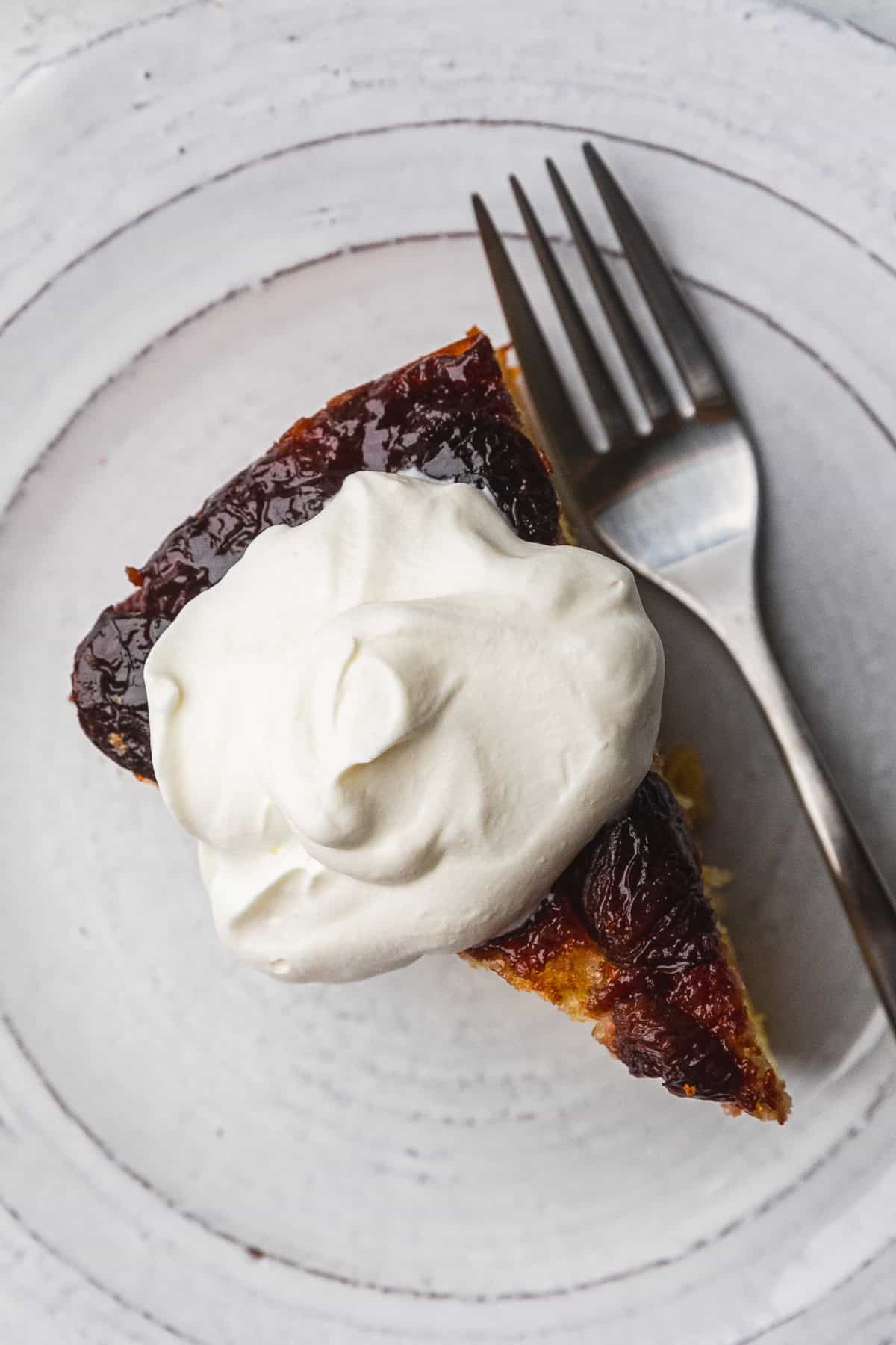 Whipped cream on top of  a slice of cherry upside down cake.