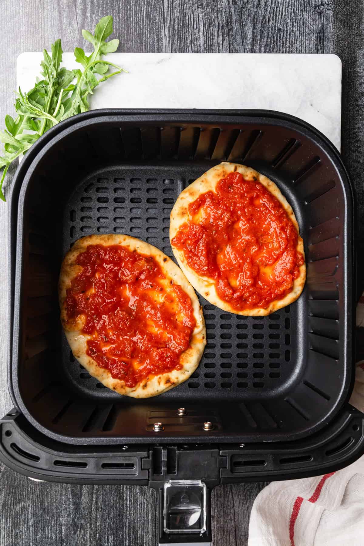 Naan bread in air fryer basket with pizza sauce.