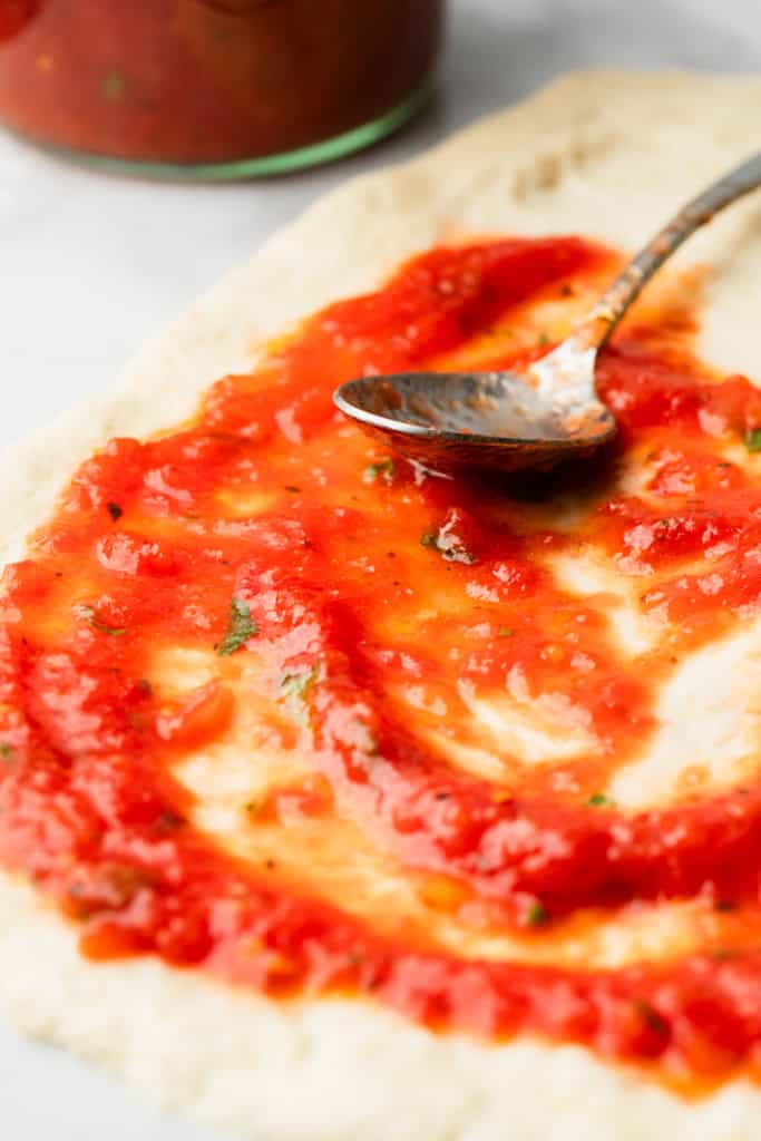 Spreading authentic pizza sauce on pizza dough.