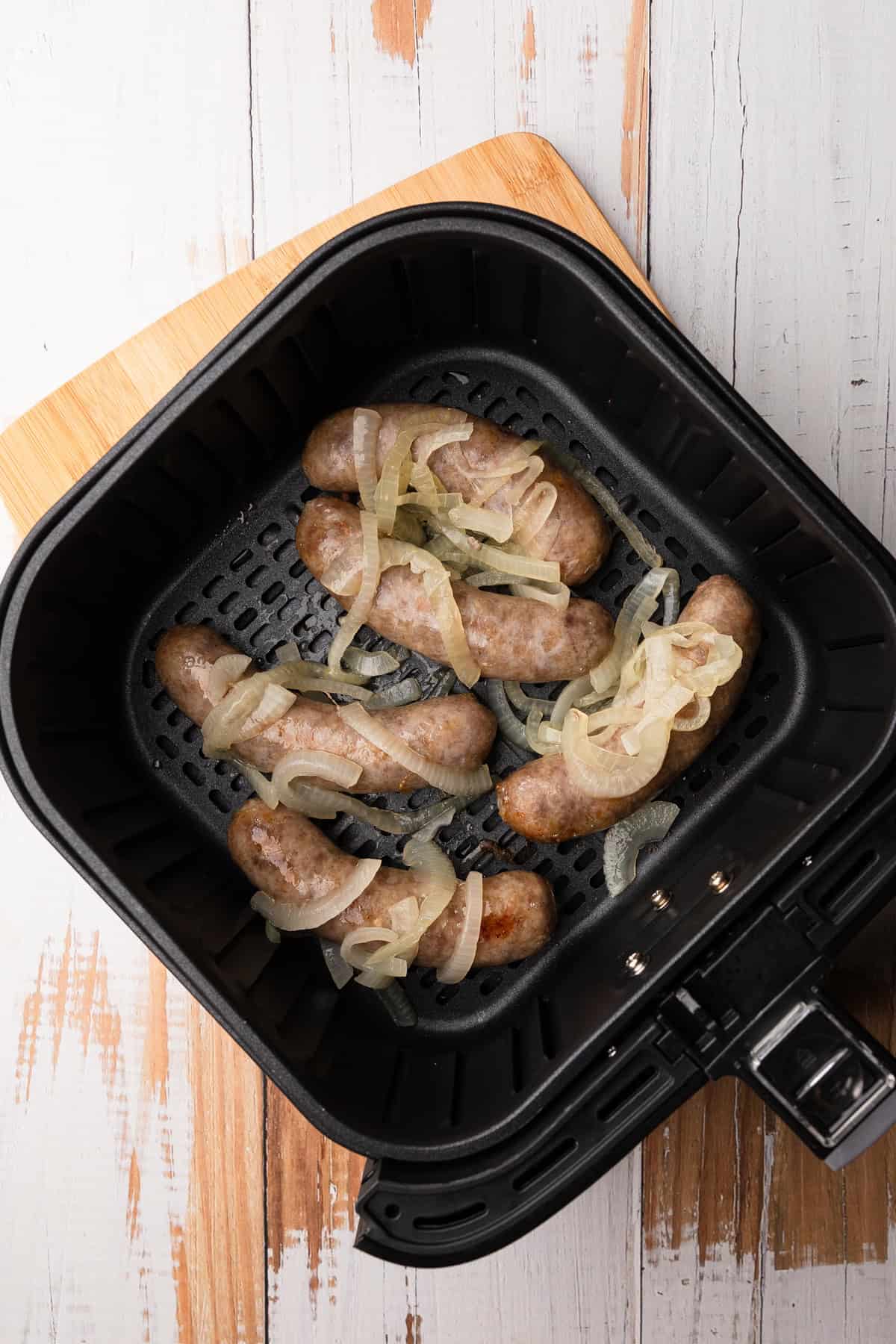 Brats cooked golden brown with onions in air fryer basket.