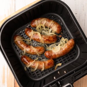 Bratwurst and onions in an air fryer basket.