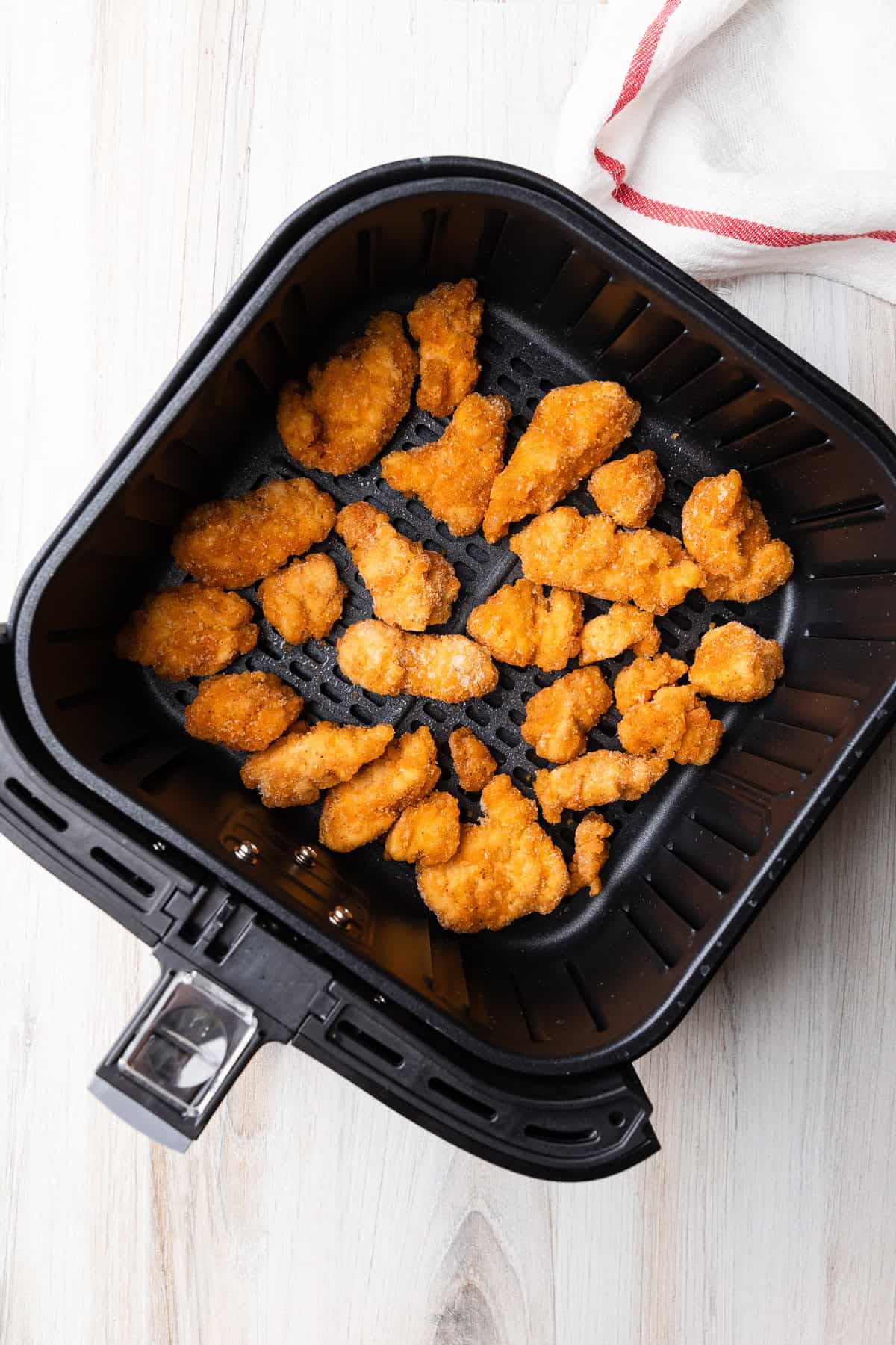 Uncooked popcorn chicken in air fryer basket.