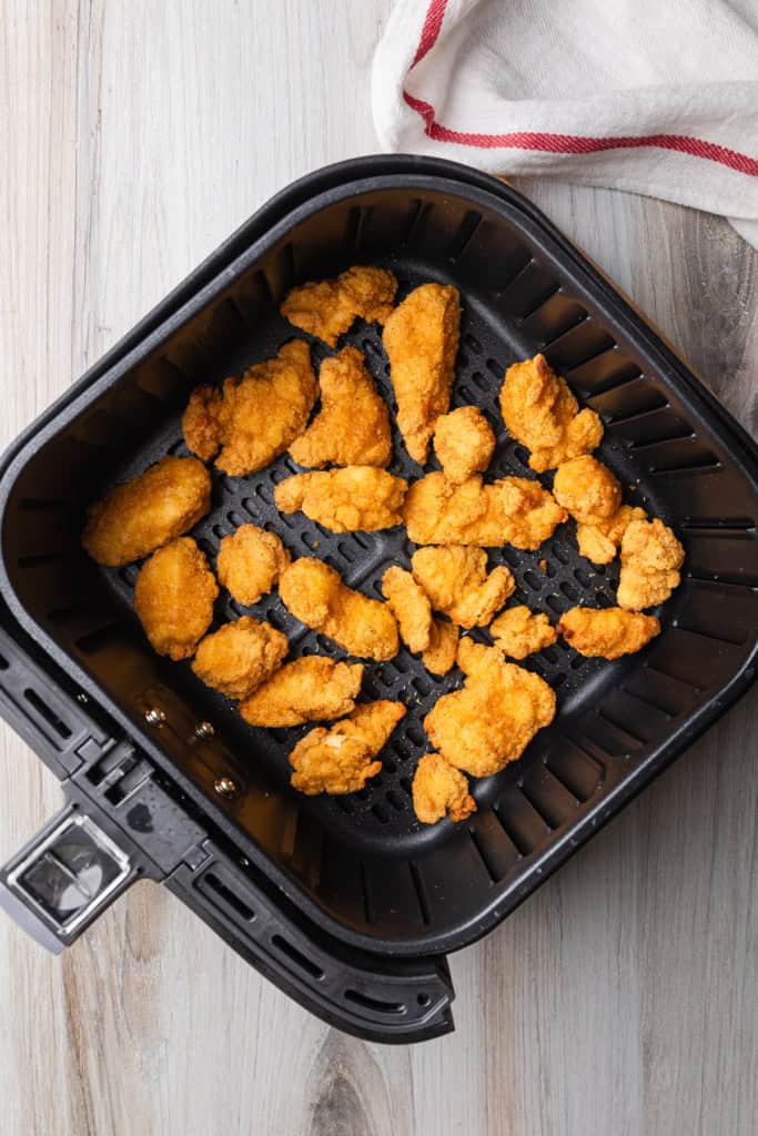 Cooked popcorn chicken in air fryer basket.