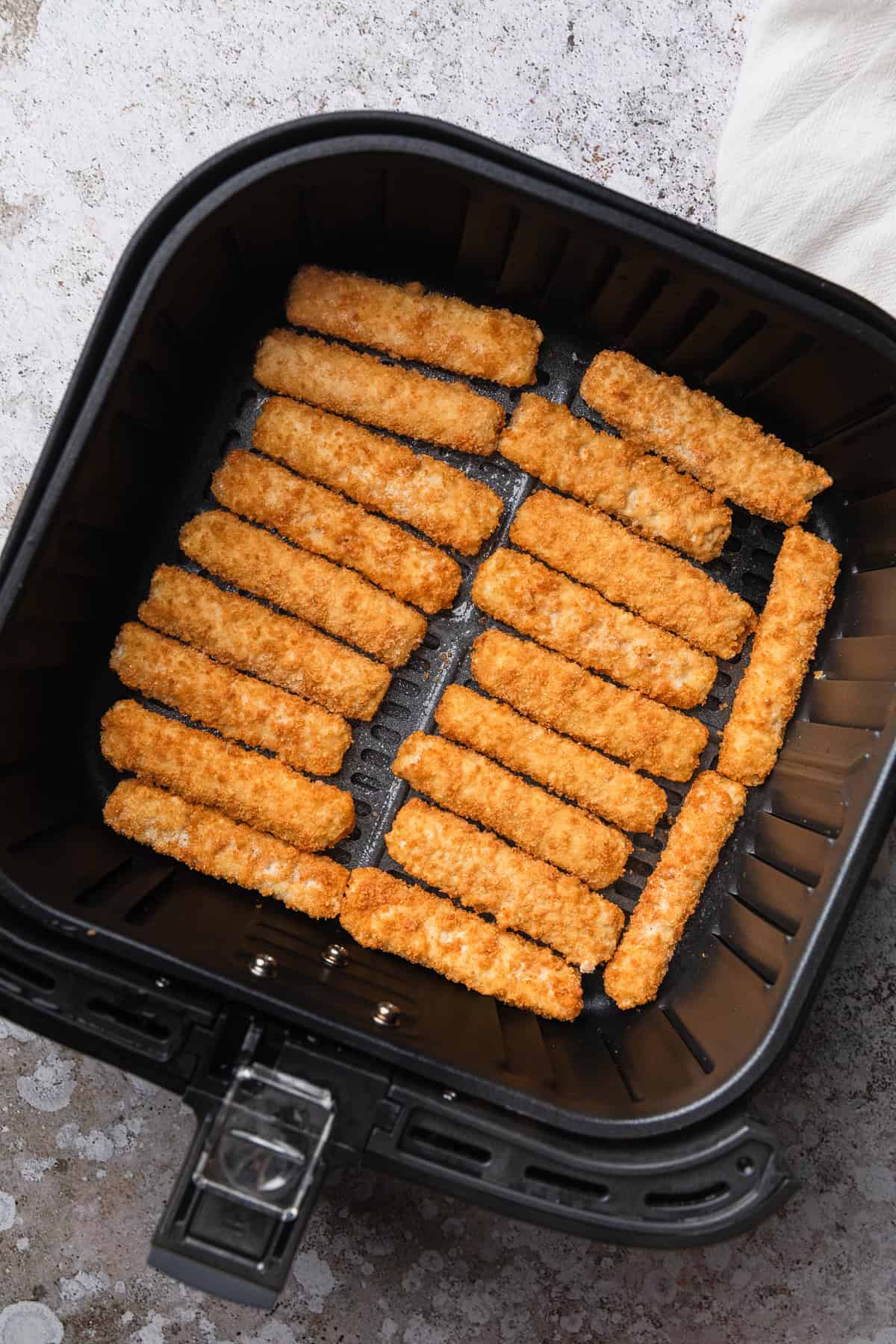 Frozen fish sticks in air fryer basket.