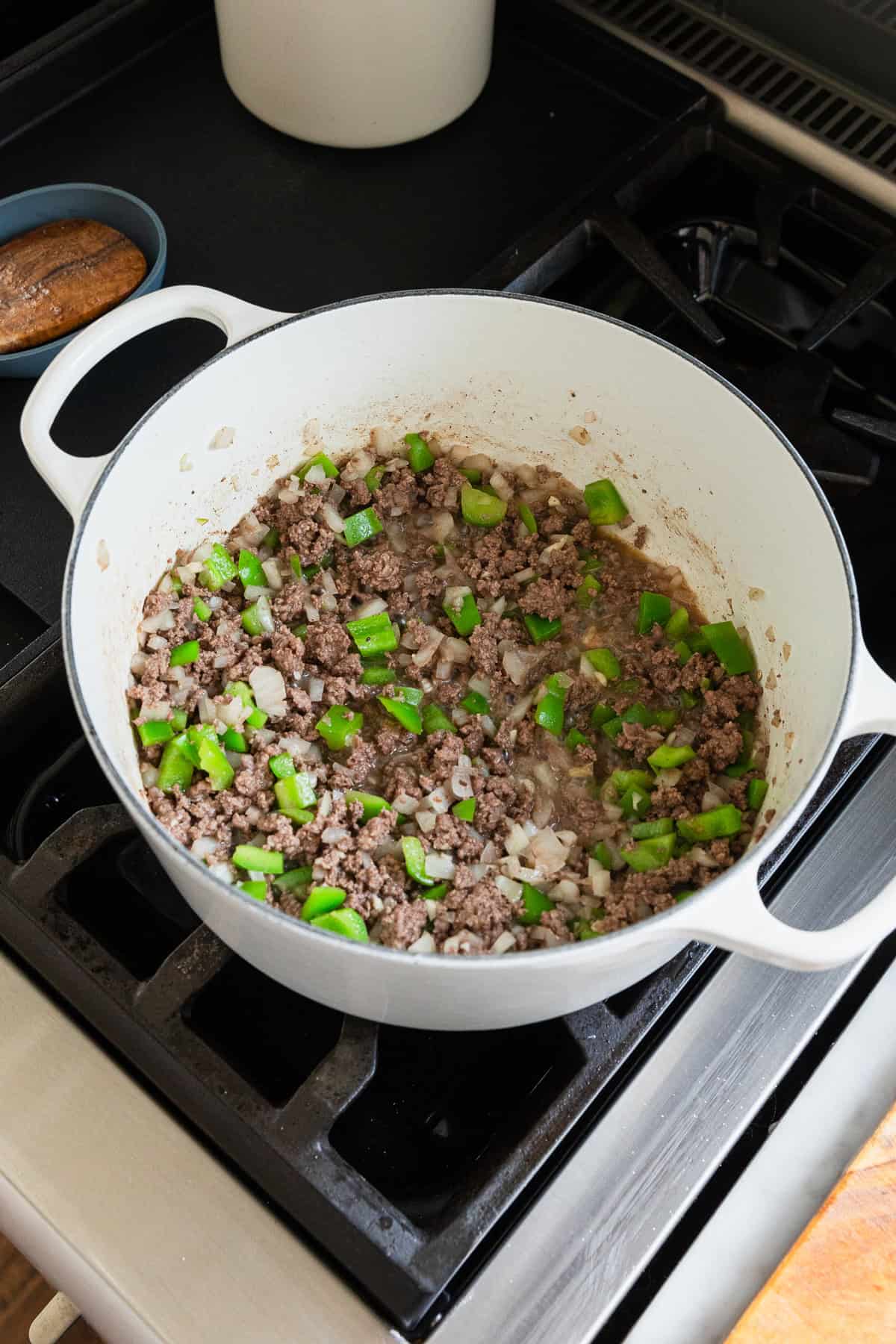 Cooking ground beef, green bell peppers, onions and garlic in a large pot.