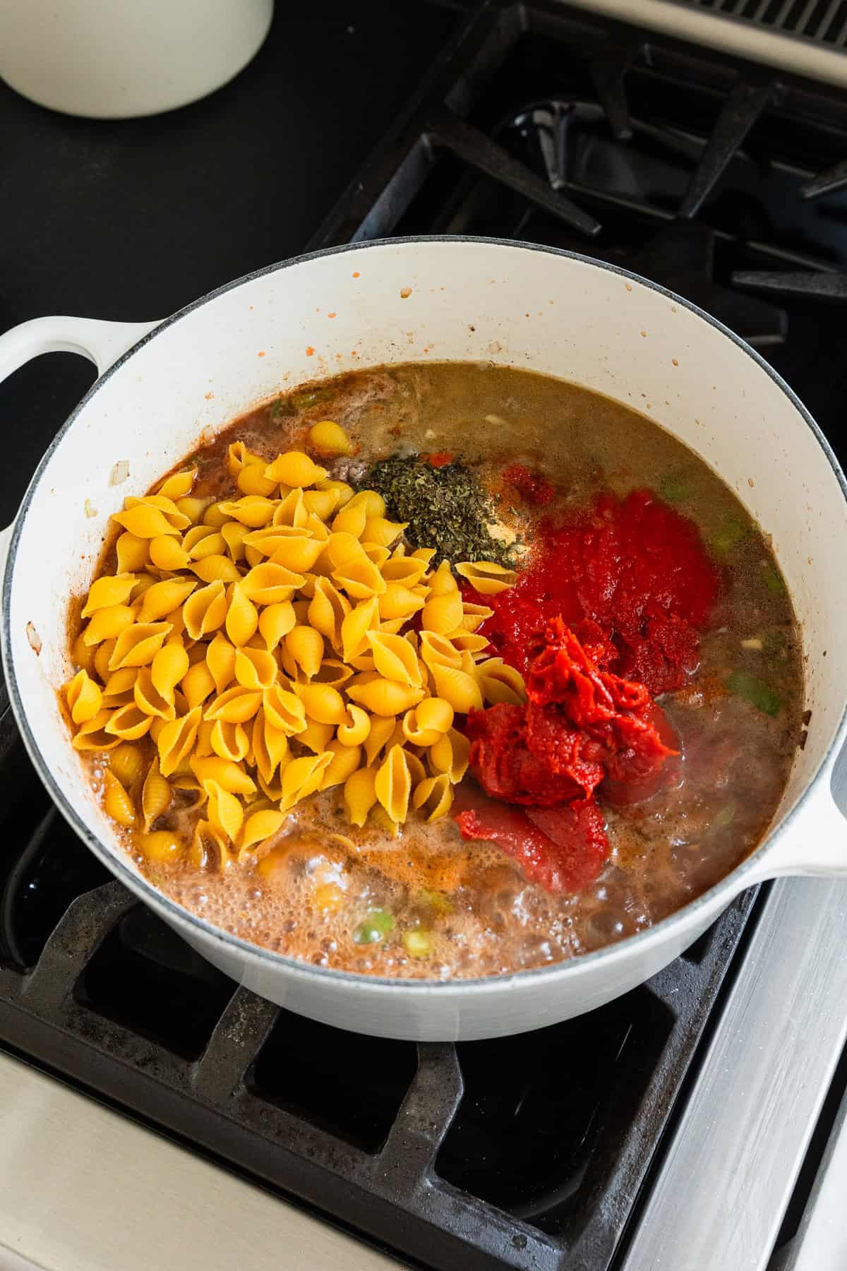 Adding sauces and dry pasta to the cooking pot.