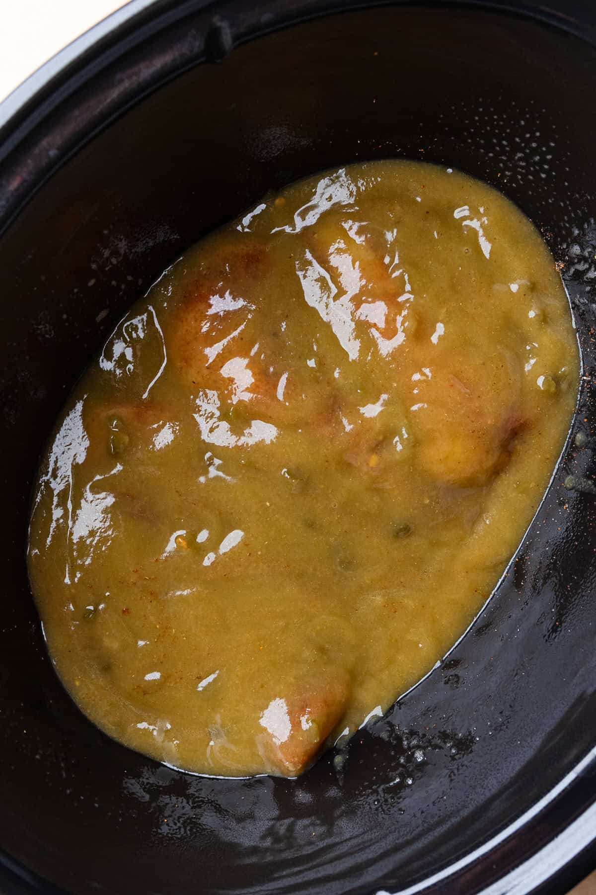 Enchilada sauce covering chicken in crockpot.