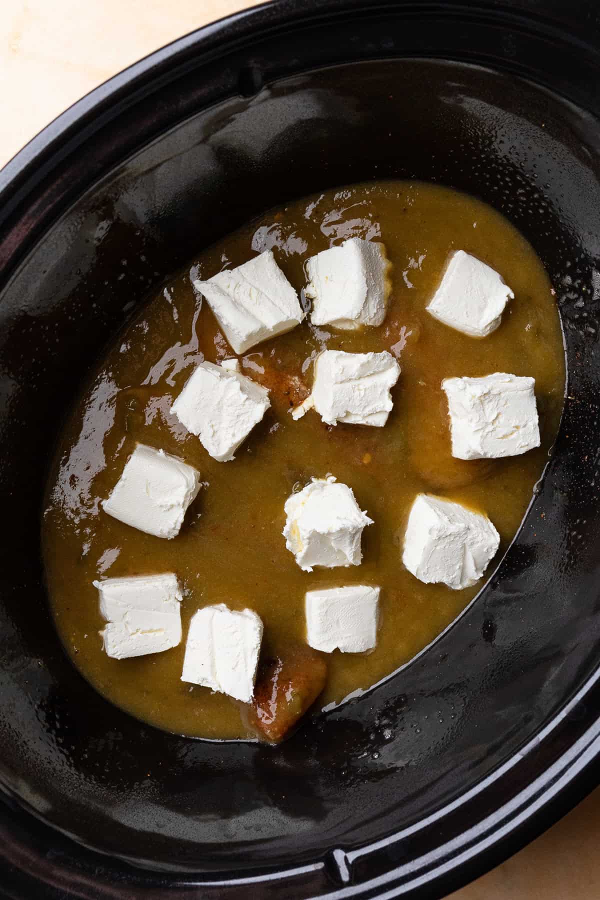 Cubes of cream cheese over the sauce in the crockpot.