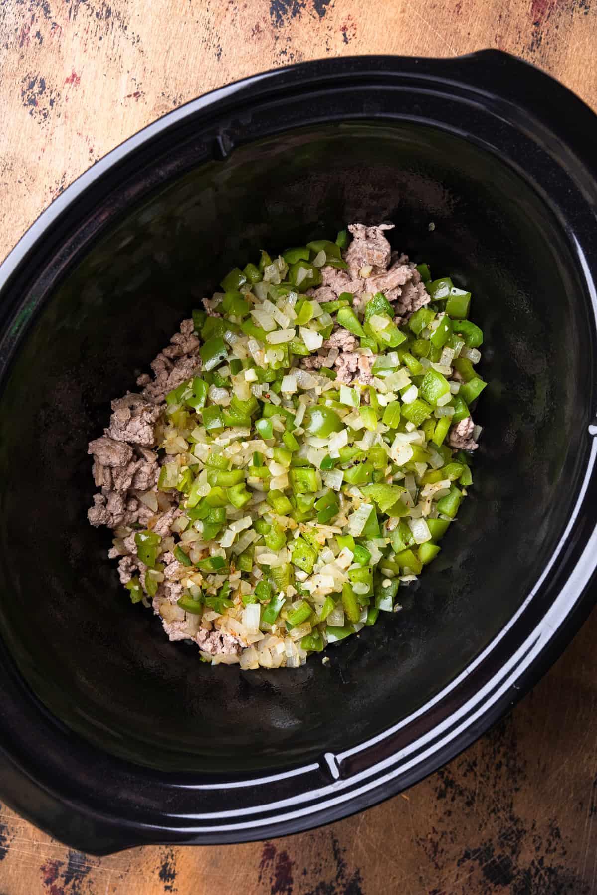 Cooked ground meat and veggies in a crockpot insert.