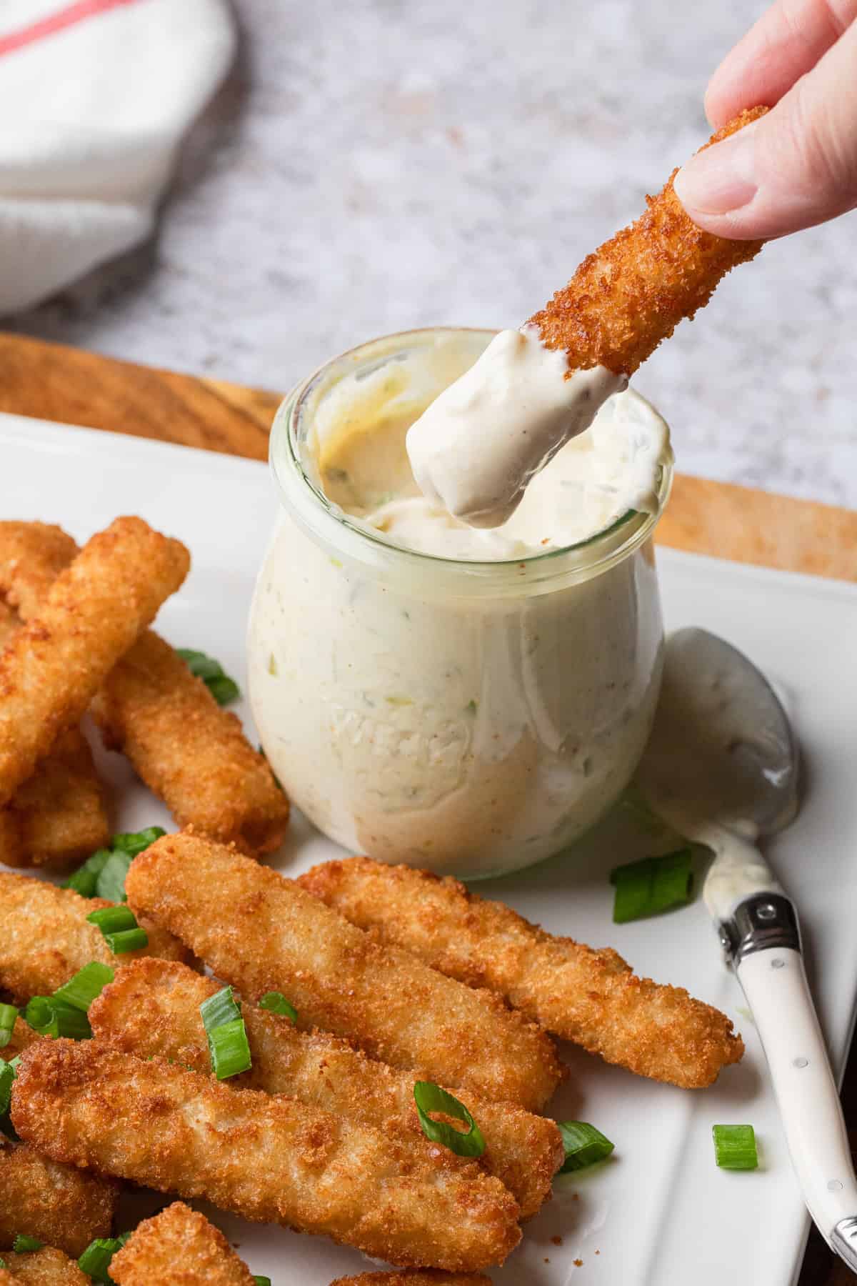 Dipping a fish stick into a jar or tartar sauce.