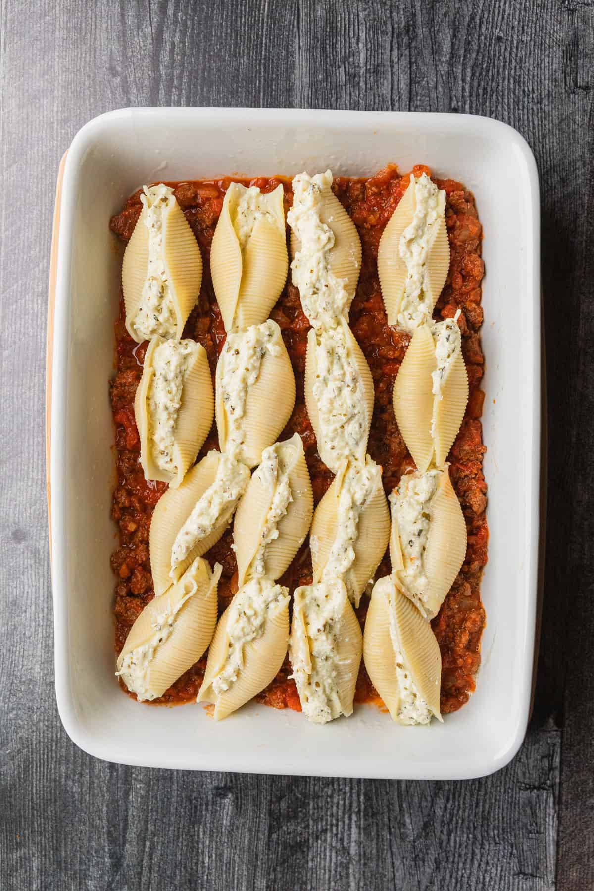 Pasta shells stuffed with ricotta in baking dish.