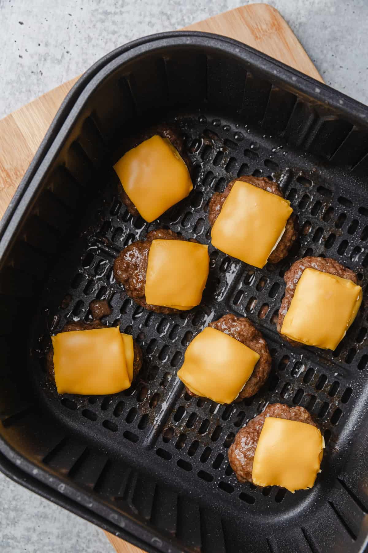 Patties in air fryer basket with melted cheese.