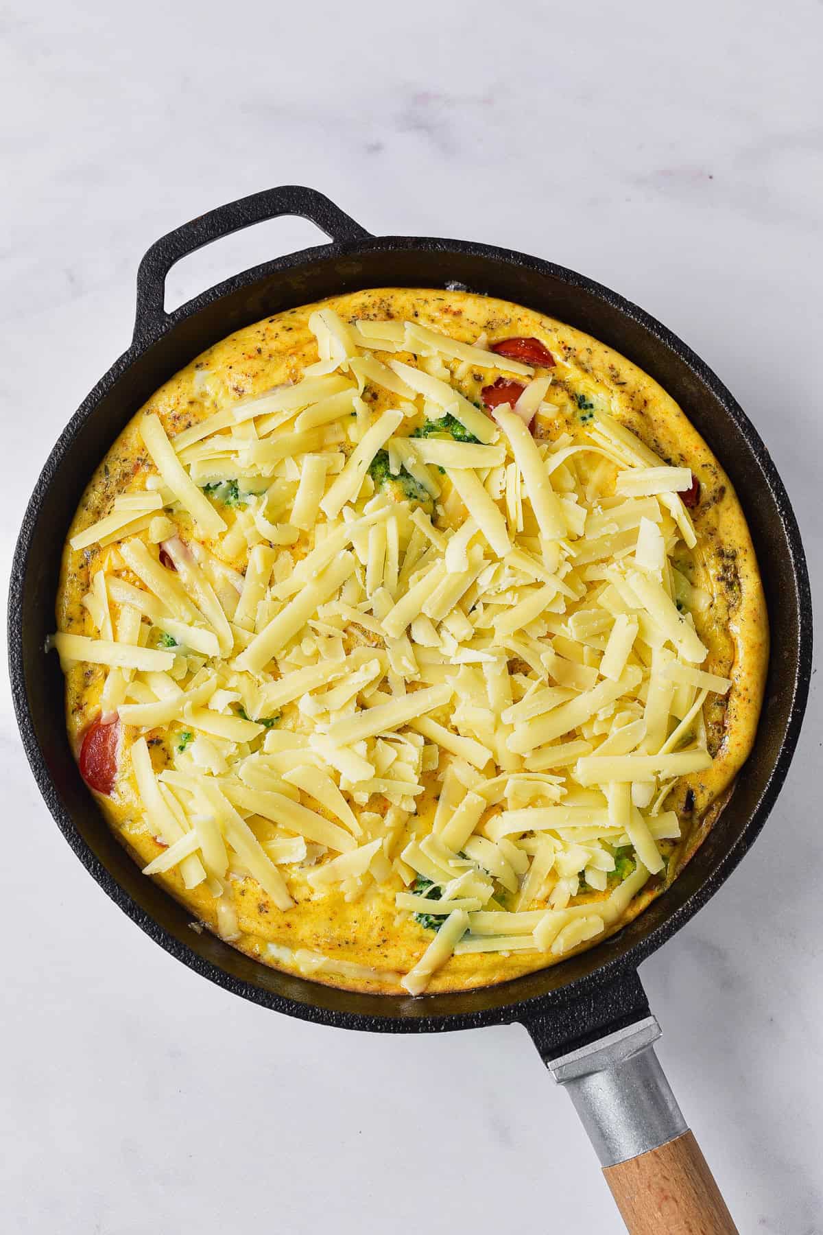 Adding cheese to partially baked frittata in skillet.