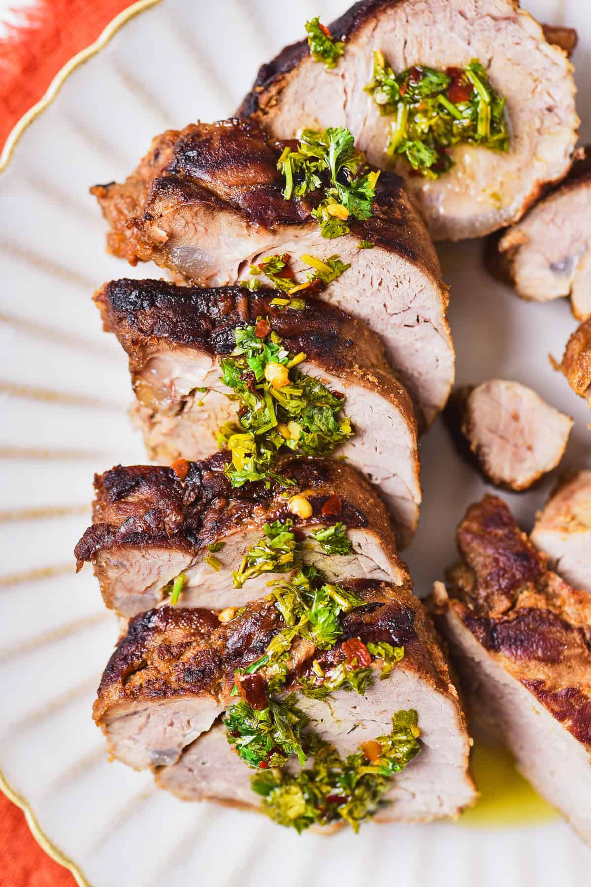 Sliced pork tenderloin on a plate with fresh herb sauce.