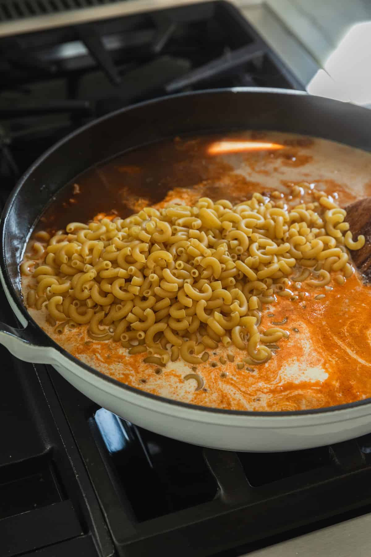 Adding macaroni and liquid ingredients to a skillet.