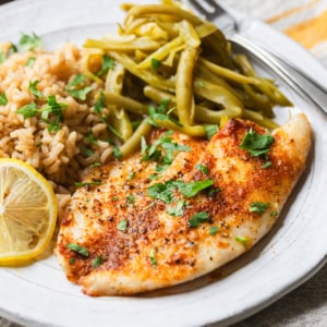 Air fryer frozen tilapia on a plate with rice and green beans.