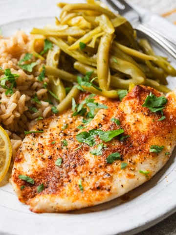 Air fryer frozen tilapia on a plate with rice and green beans.