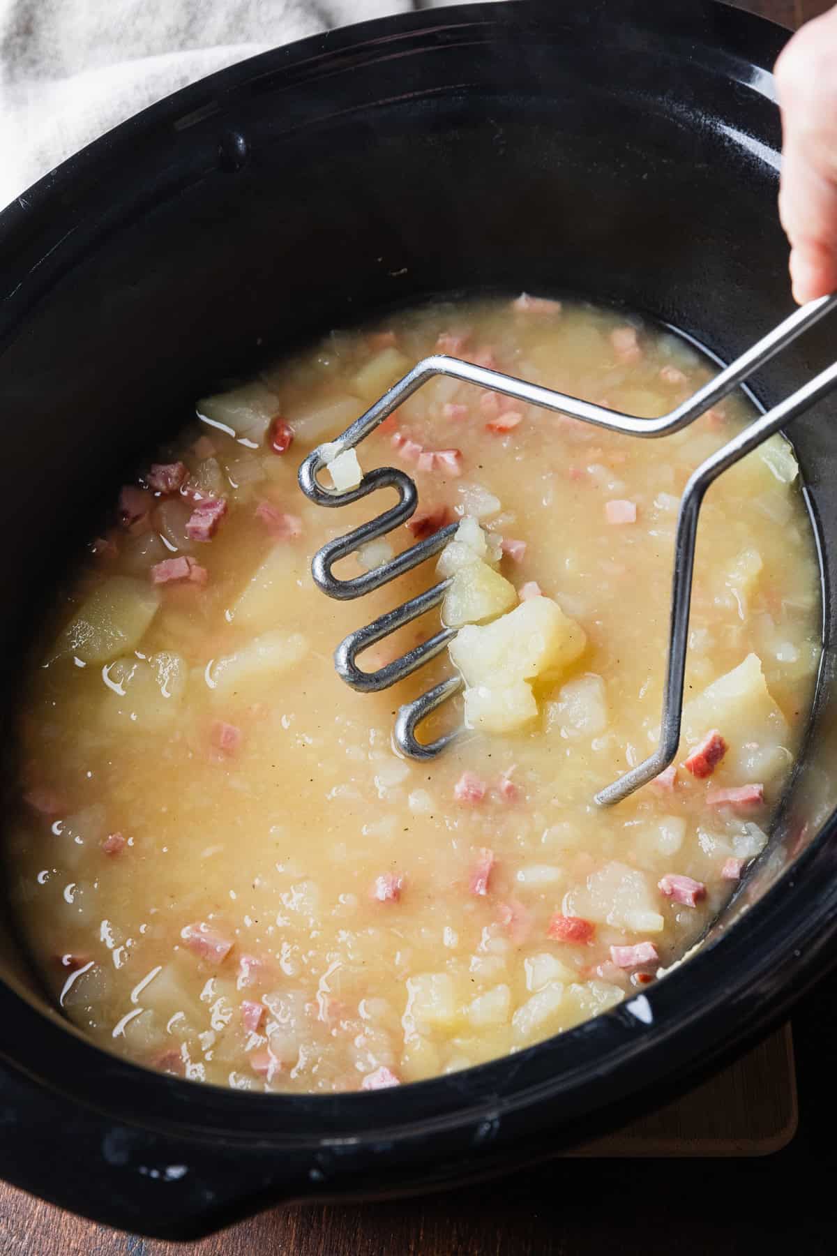 Using a potato masher to make a chunky soup.