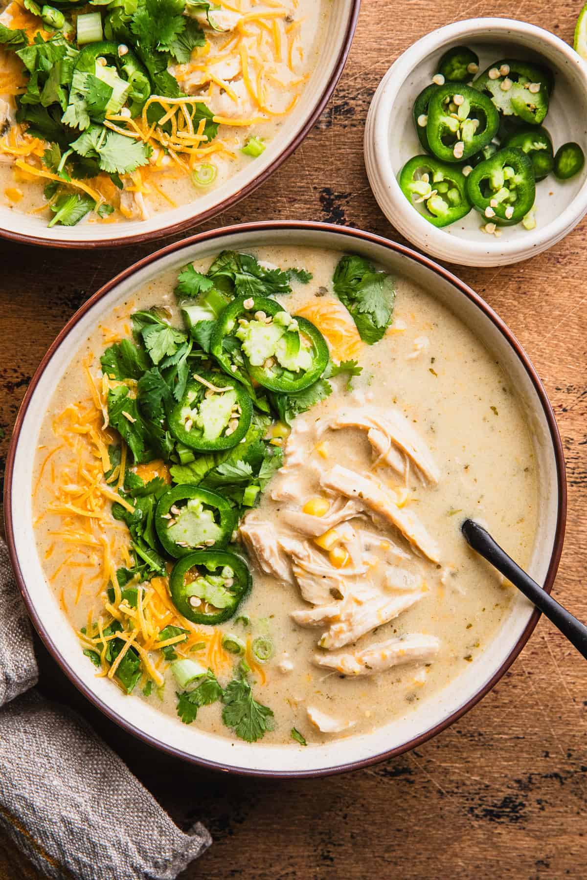 Green chile chicken soup in a bowl with cilantro and sliced jalapeno peppers.