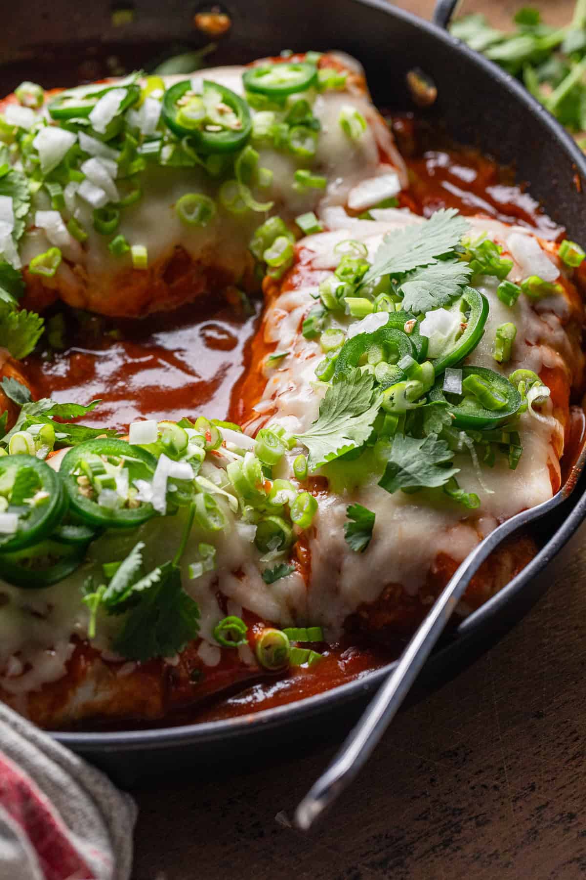 Completed smothered burritos in a red sauce in the skillet.