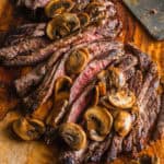 A sliced flank steak with mushrooms on a cutting board.