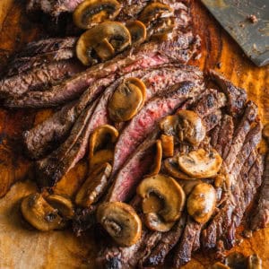 A sliced flank steak with mushrooms on a cutting board.