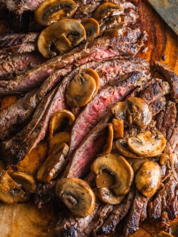 A sliced flank steak with mushrooms on a cutting board.