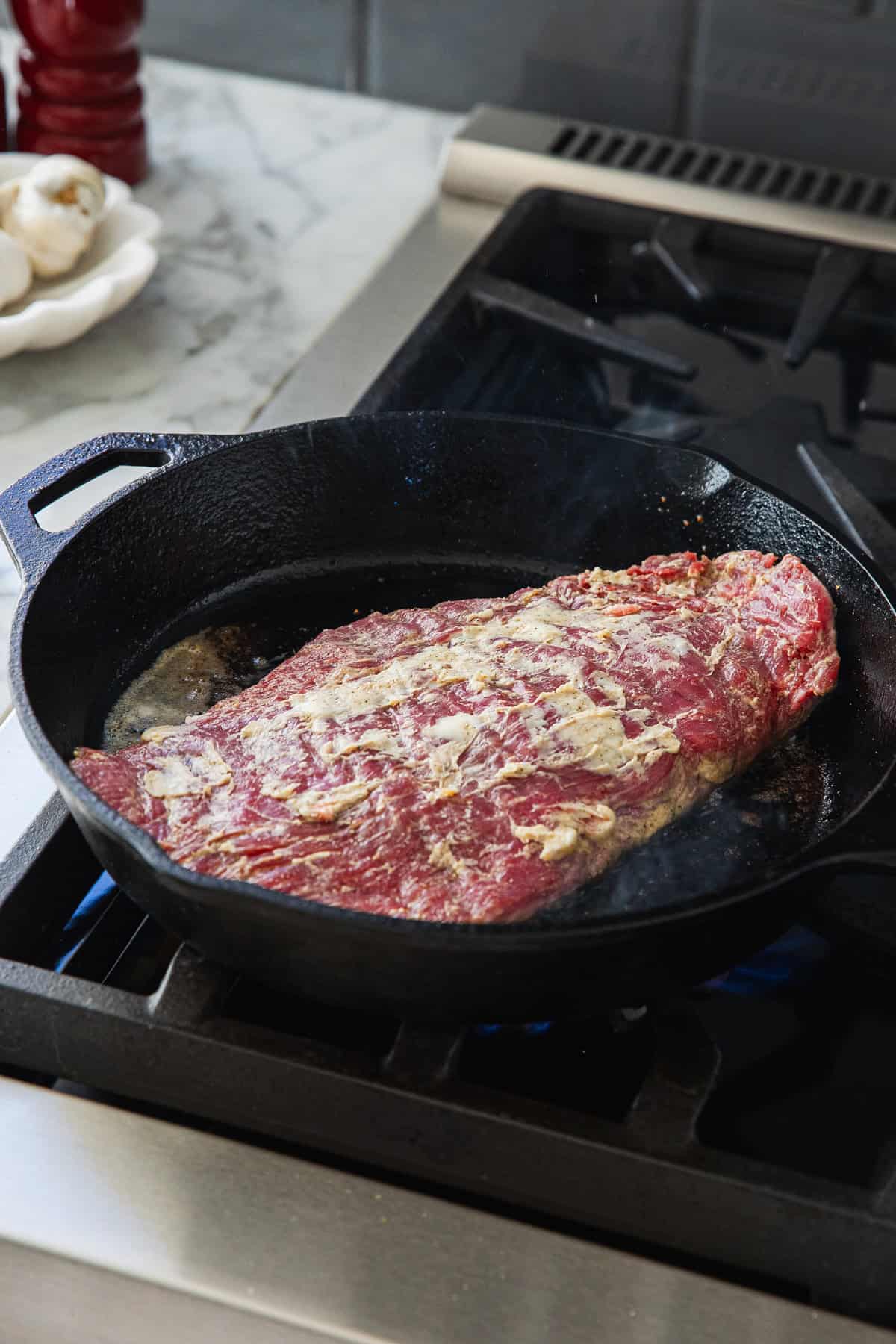 Adding raw steak to cast iron pan.