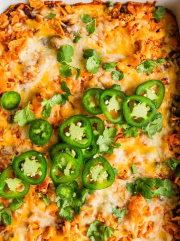 Ground beef Doritos nachos casserole in a white baking dish with garnishes.