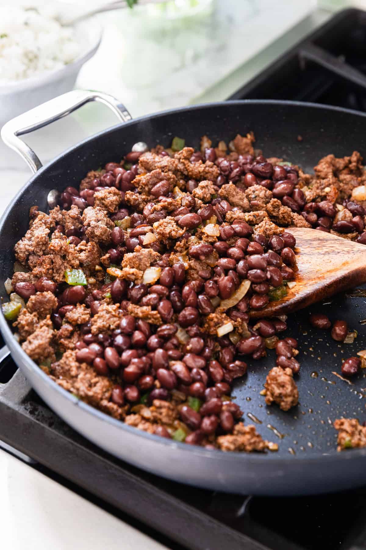 Adding black beans to the skillet to make the recipe.