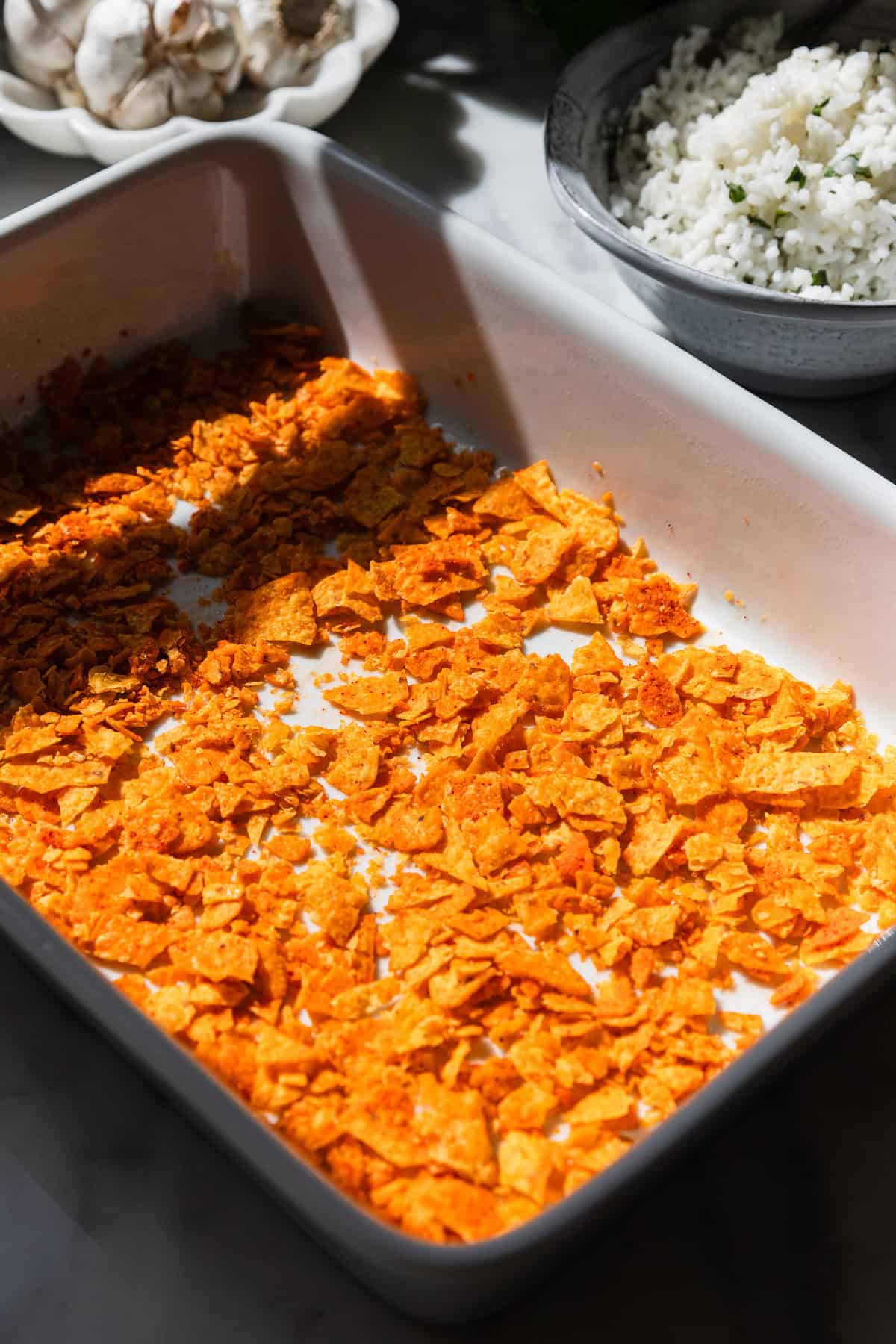 Adding crushed doritos to a baking dish.