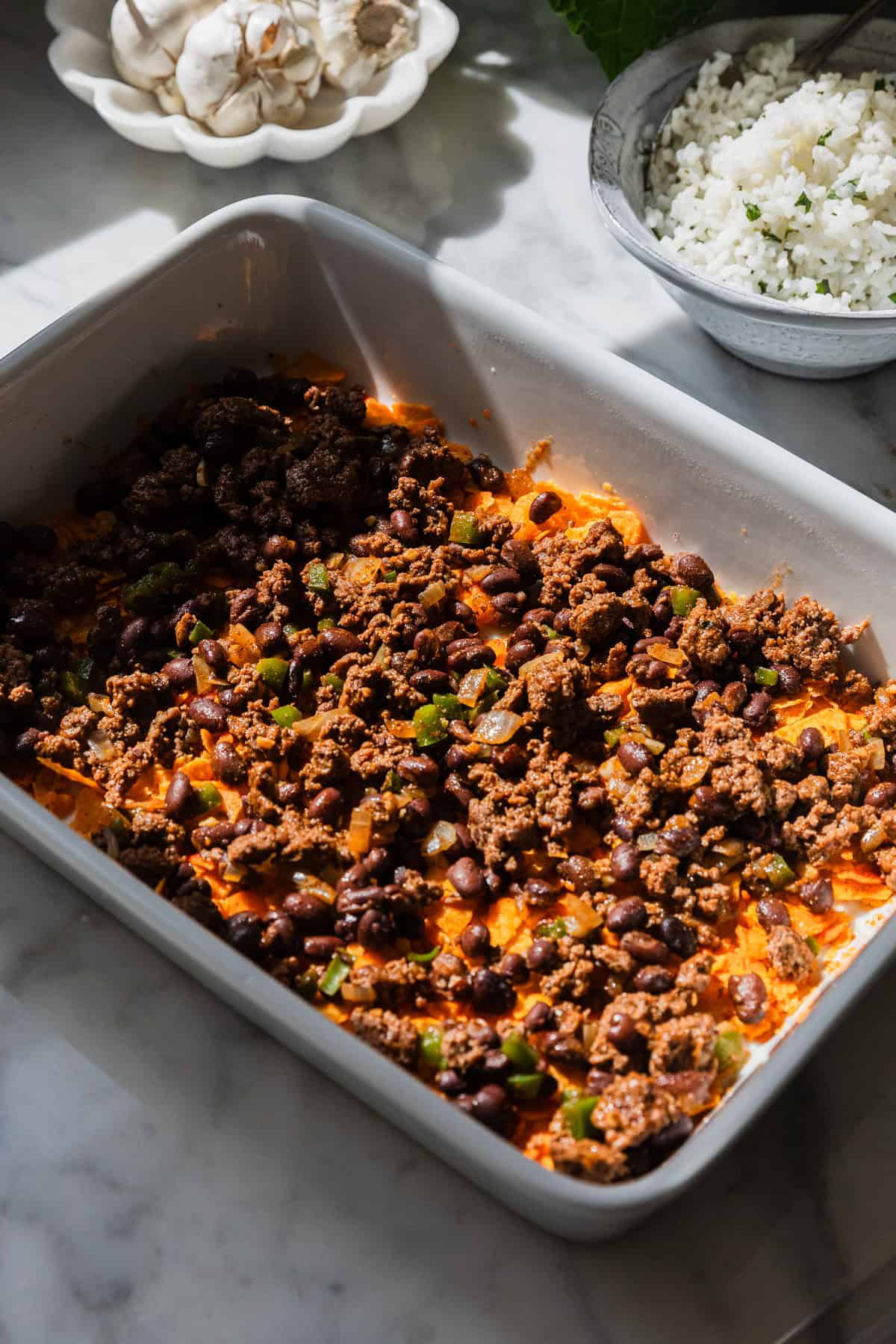 Adding meat mixture over  crushed doritos in the baking dish.