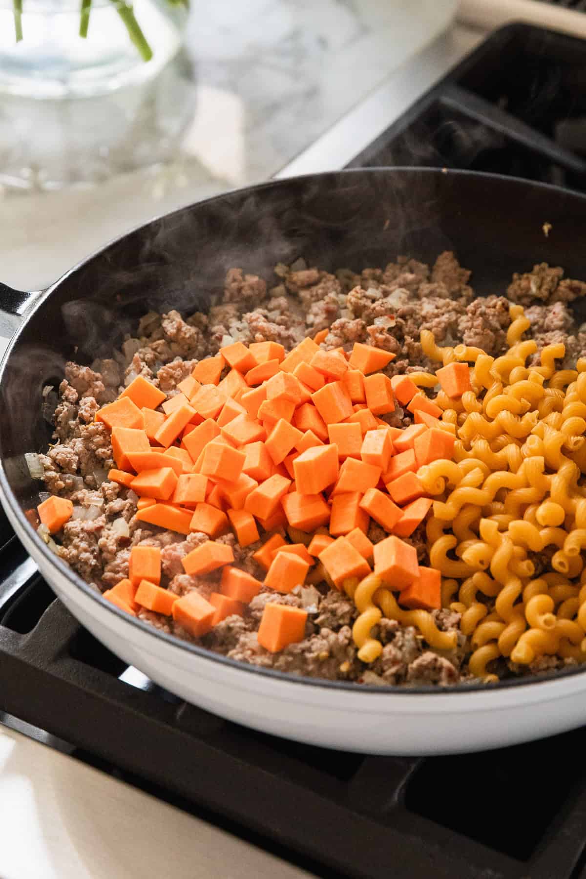 Adding sweet potatoes and pasta to skillet.