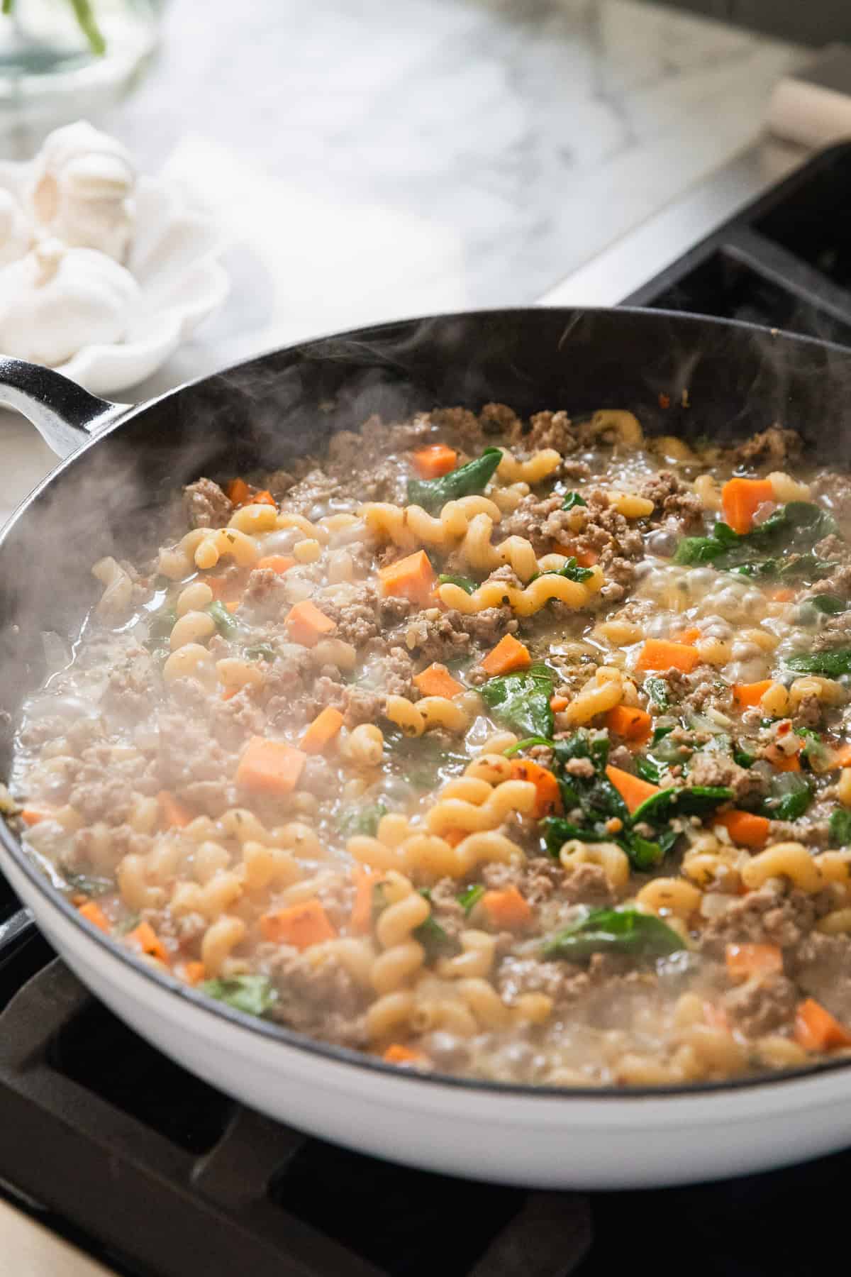 Adding chicken broth to the skillet to cook the ingredients.