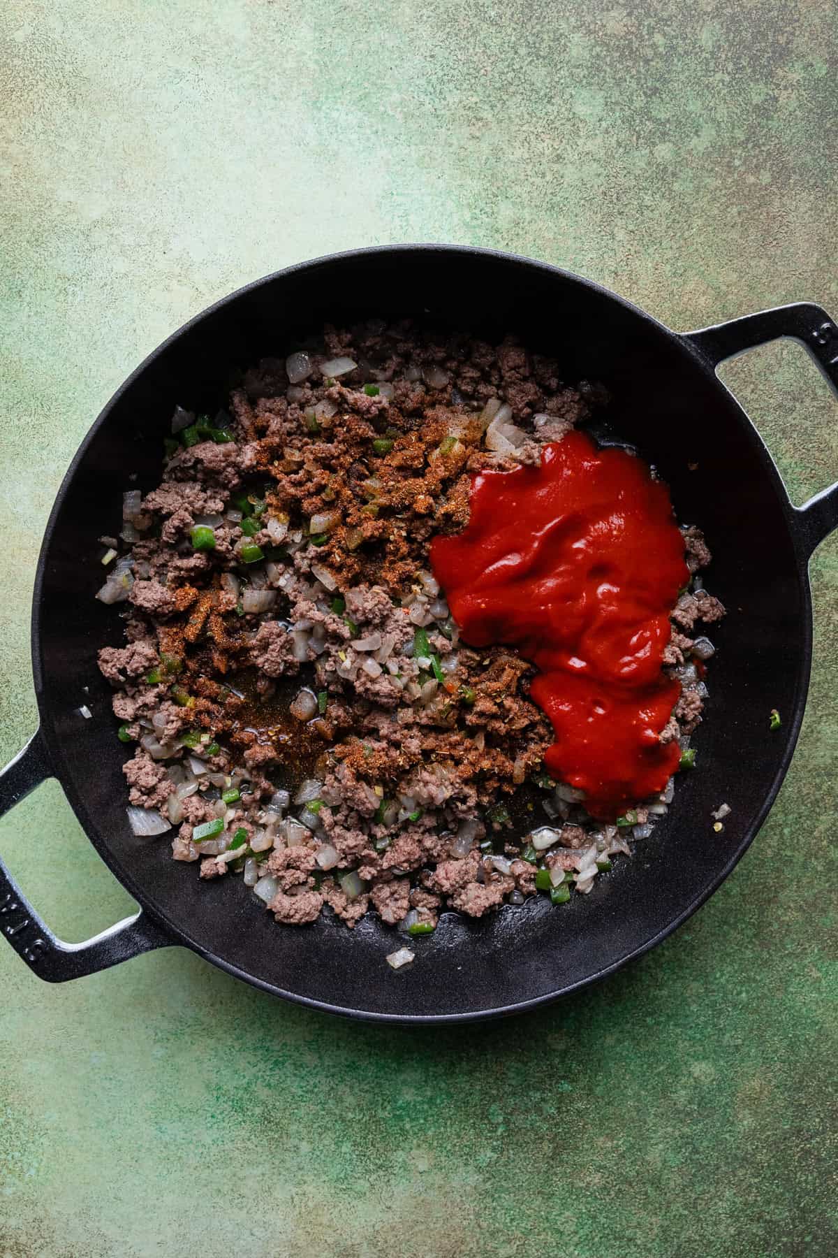 Adding red chile sauce to the skillet to make beef and potatoes.