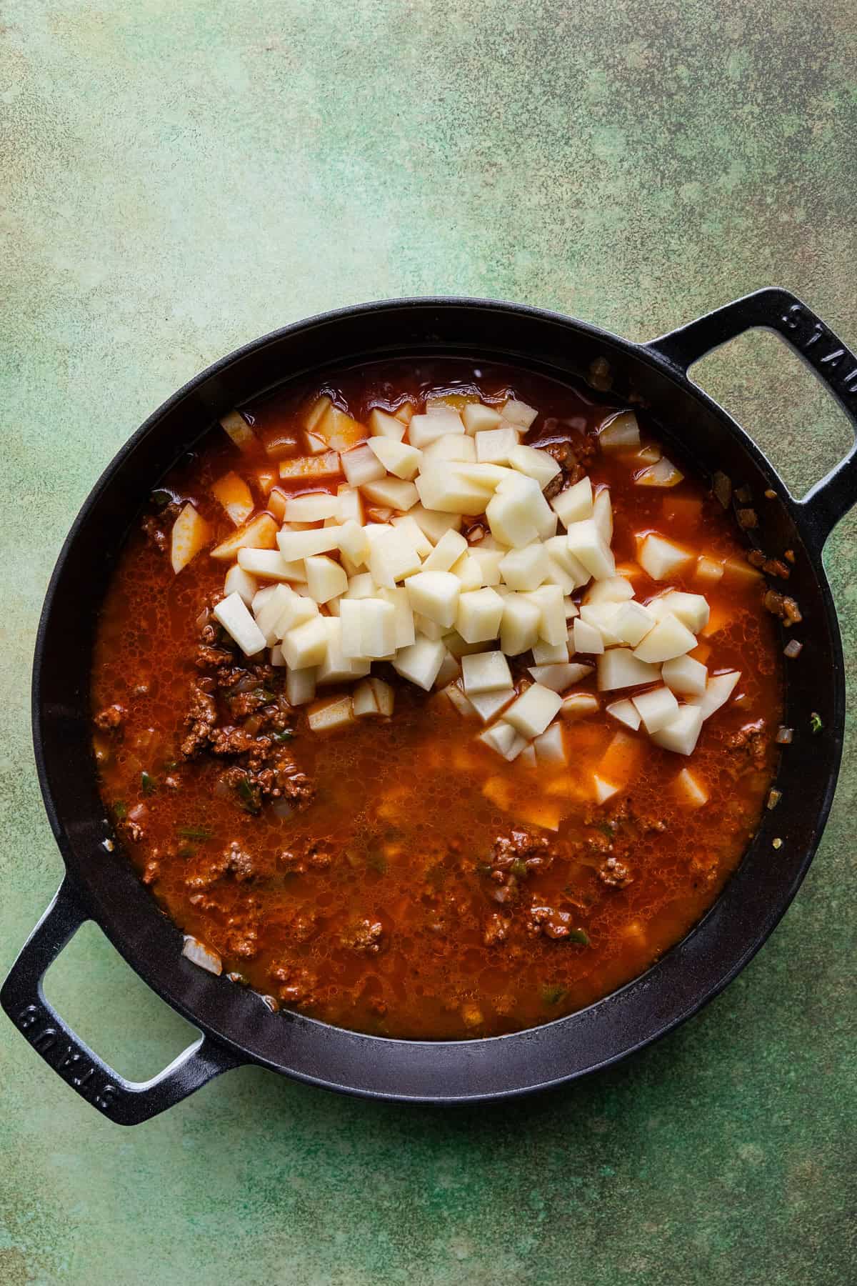 Adding uncooked potatoes to the skillet.